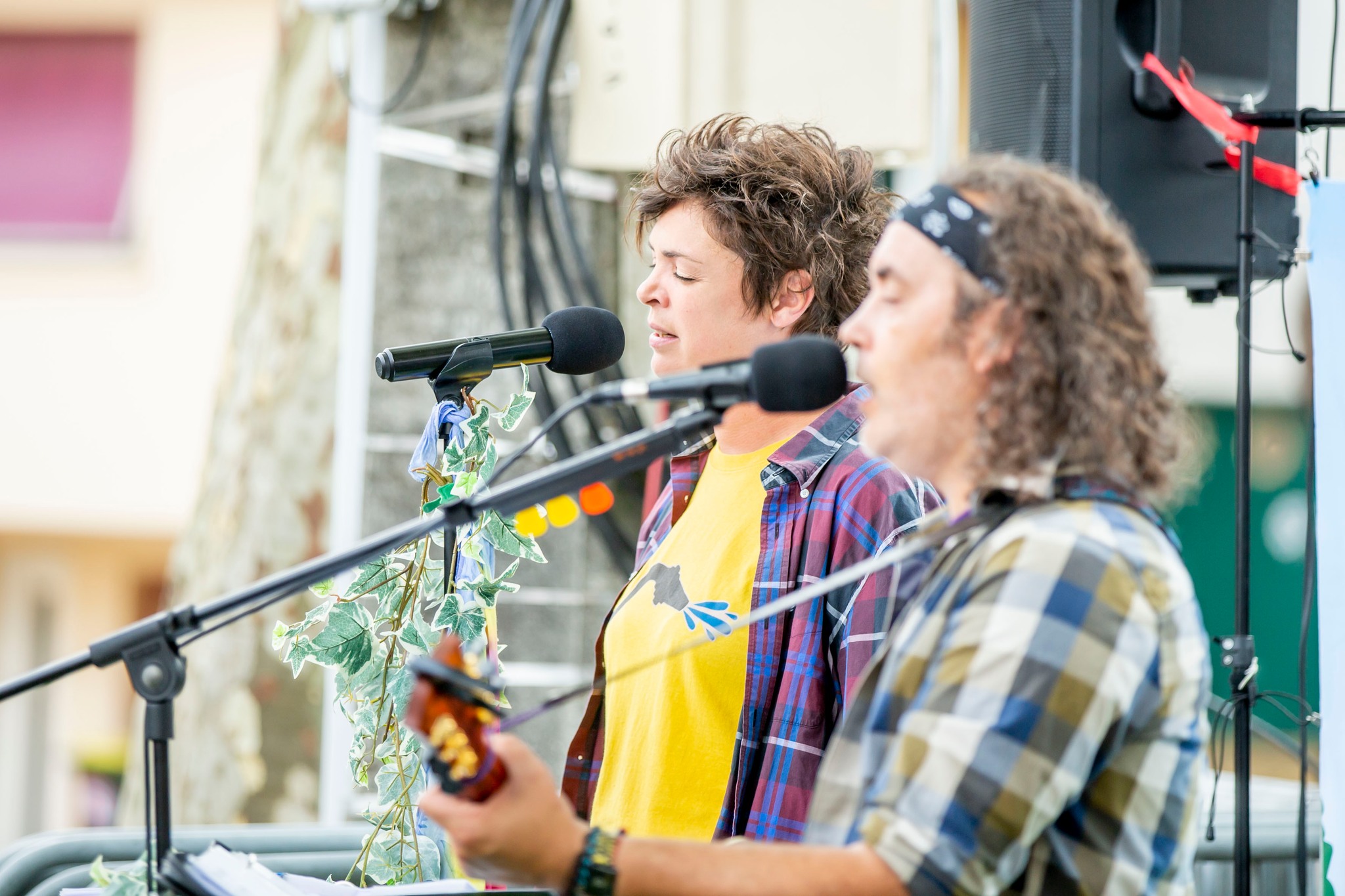 Muriel et Joan en concert en plein air, chantant au micro avec leurs instruments.